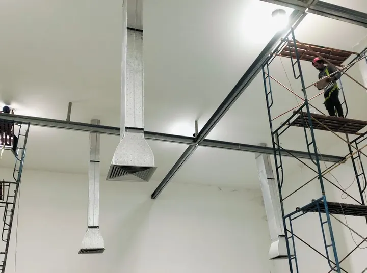 Ducting galvanis menggantung dari rangka baja plafon, dipasang dengan scaffolding