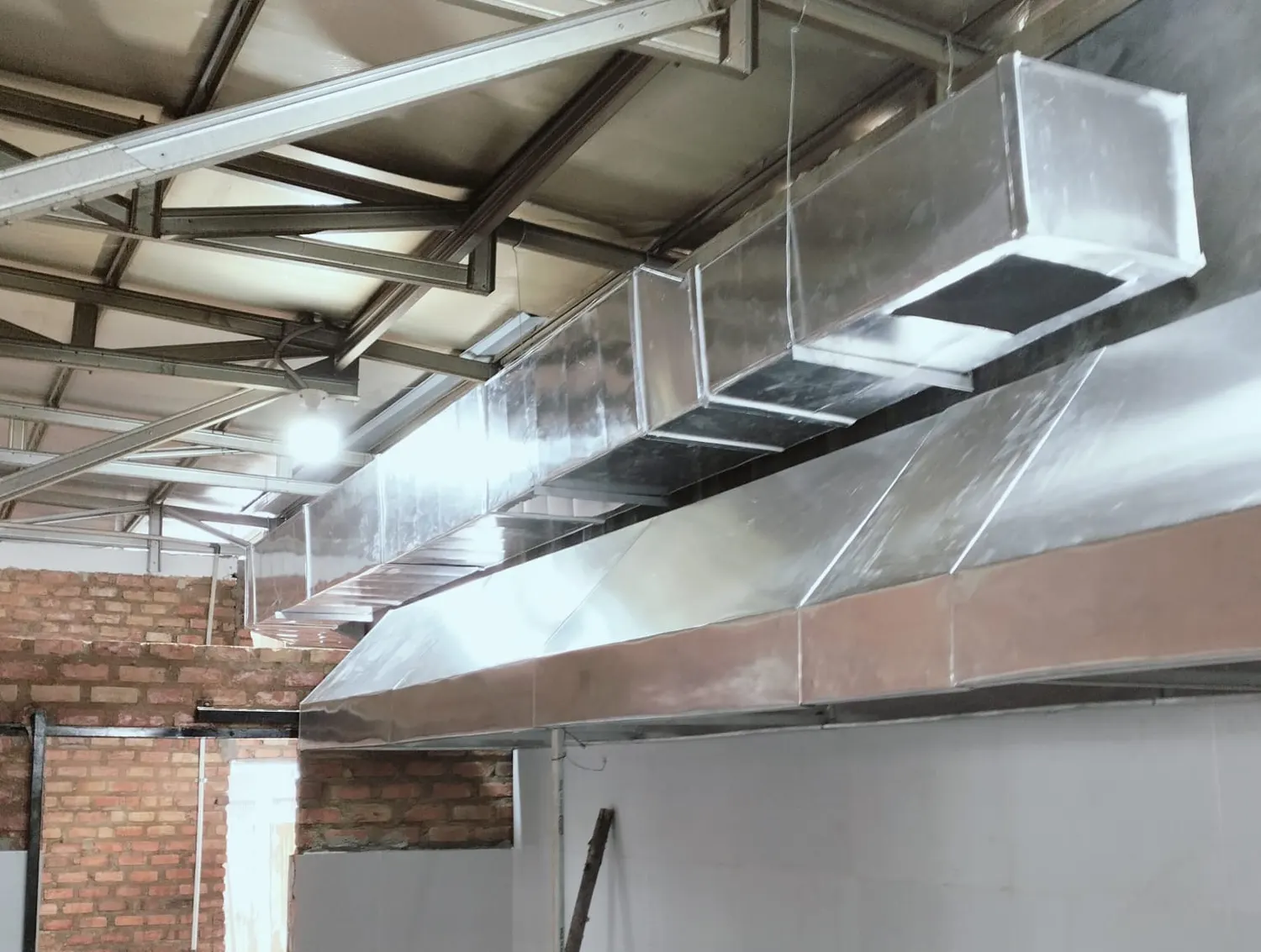 Kitchen hood panjang dari plat galvanis dengan saluran exhaust di bawah atap baja, di dapur berdinding bata