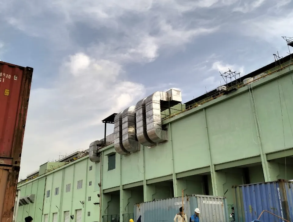 Deretan saluran exhaust galvanis besar di atap bangunan pabrik berdinding hijau